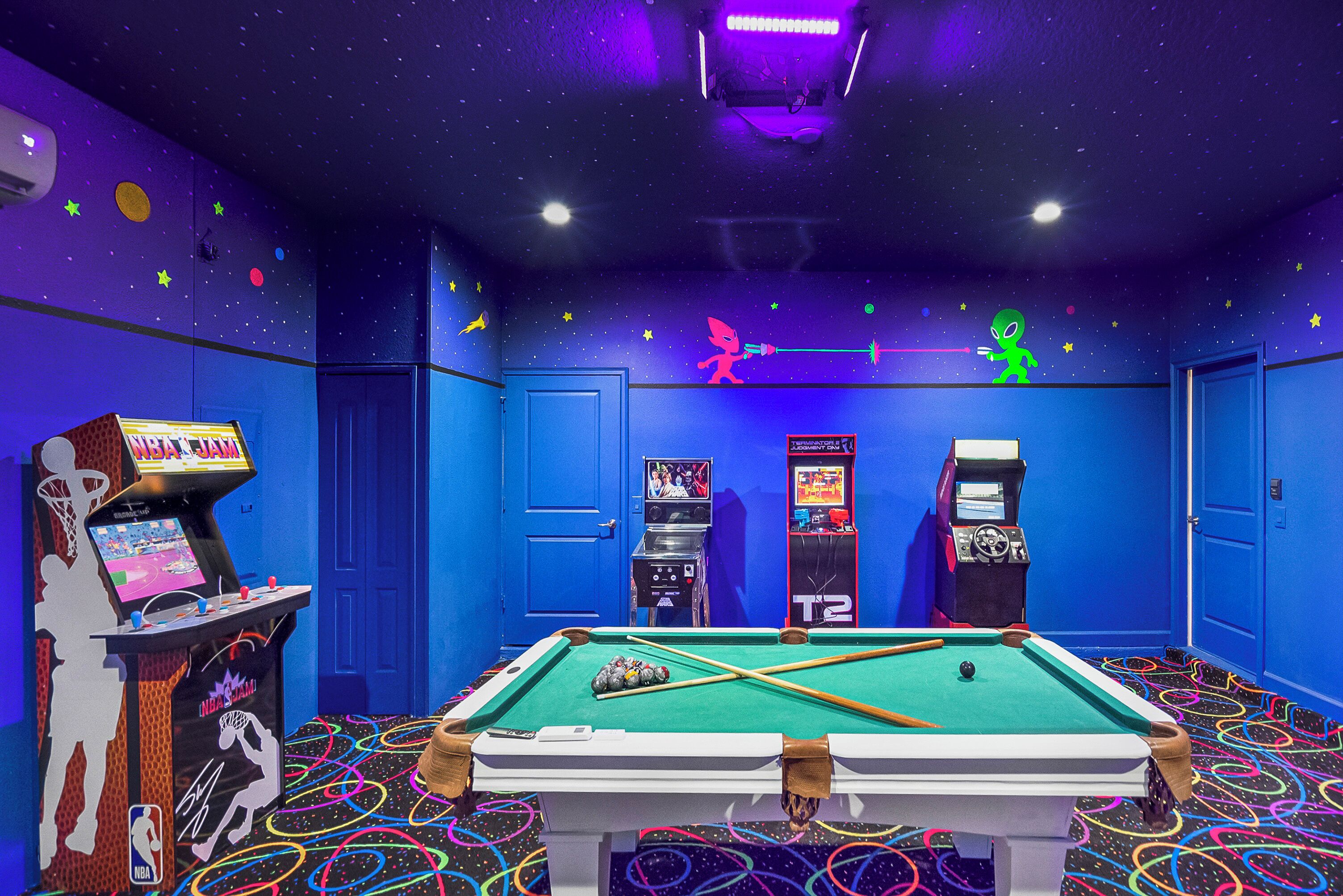 A pool table in a room with blue walls, arcade games, and a starry ceiling.