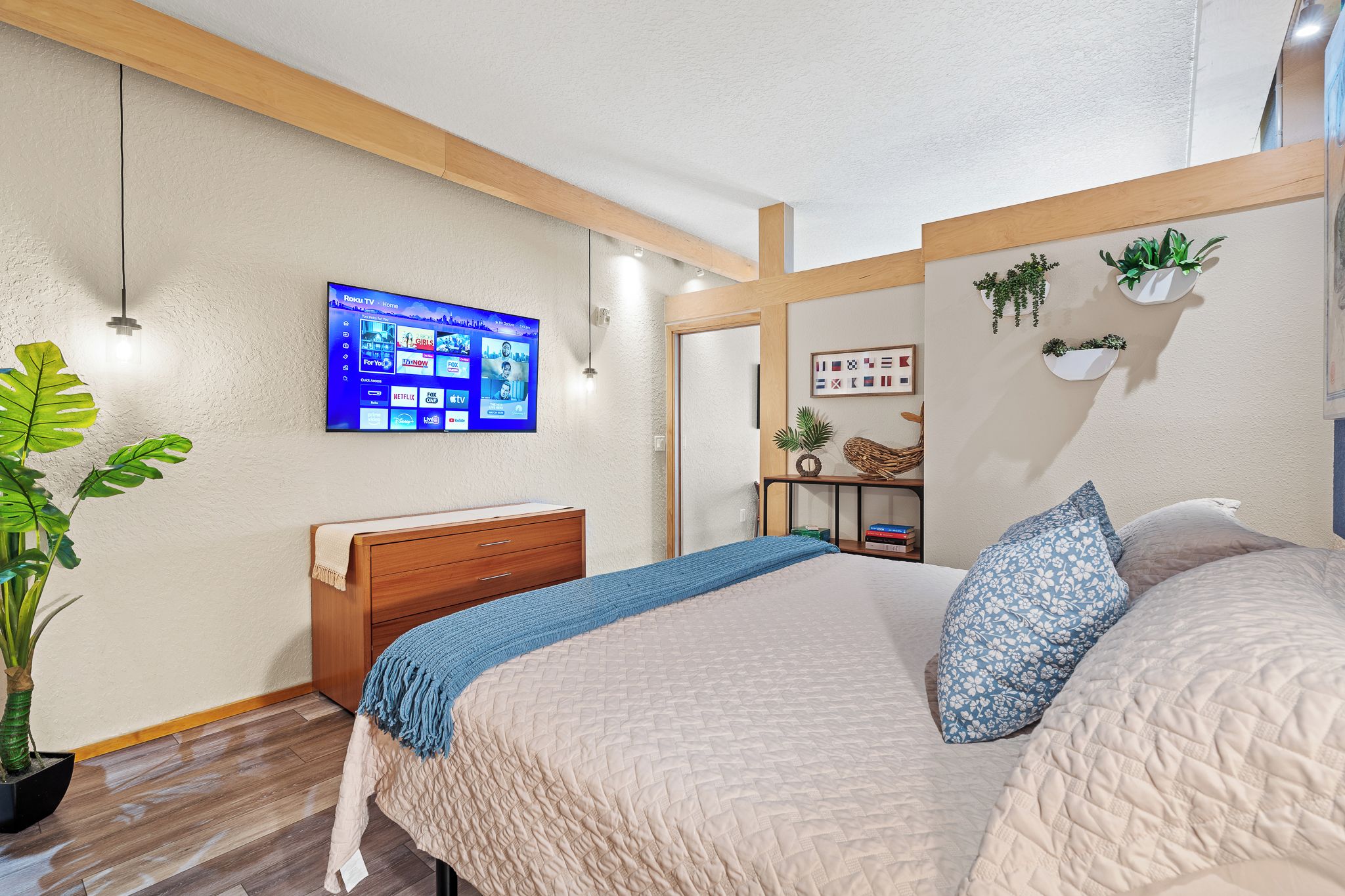 Een slaapkamer met een bed, een dressoir, een aan de muur bevestigde televisie en een plant.