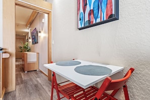 Ein Essbereich mit einem weißen Tisch und roten Stühlen, einem gerahmten abstrakten Gemälde an der Wand und einem Holzschrank mit einer Pflanze.
