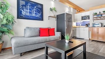 Una sala de estar moderna con un sofá gris, cojines rojos, una mesa de centro negra y una gran obra de arte con un plano azul en la pared.
