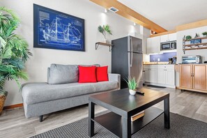 Una sala de estar moderna con un sofá gris, cojines rojos, una mesa de centro negra y una gran obra de arte con un plano azul en la pared.