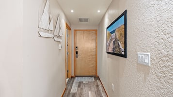 Un pasillo con una puerta de madera, un cuadro enmarcado de una playa e interruptor de luz en la pared.