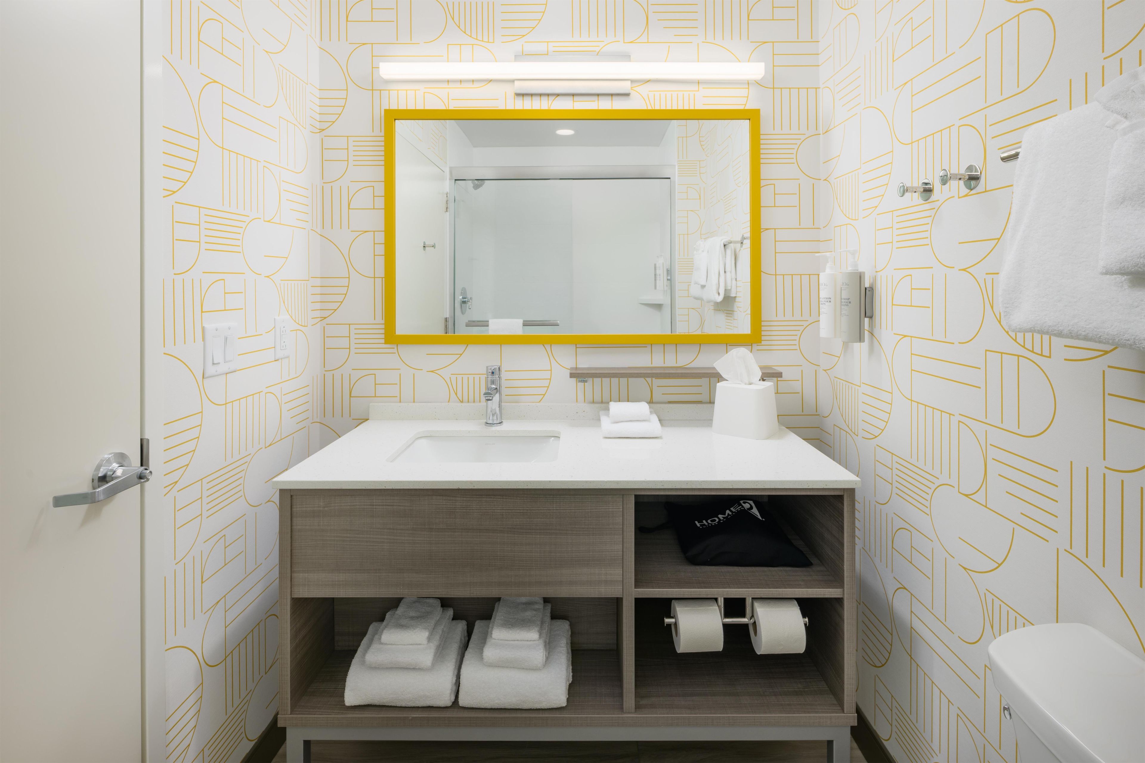 Un baño moderno con lavamanos, espejo y retrete blancos. Hay toallas y artículos de aseo en el lavamanos y el retrete.