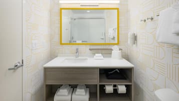 Un baño moderno con lavamanos, espejo y retrete blancos. Hay toallas y artículos de aseo en el lavamanos y el retrete.