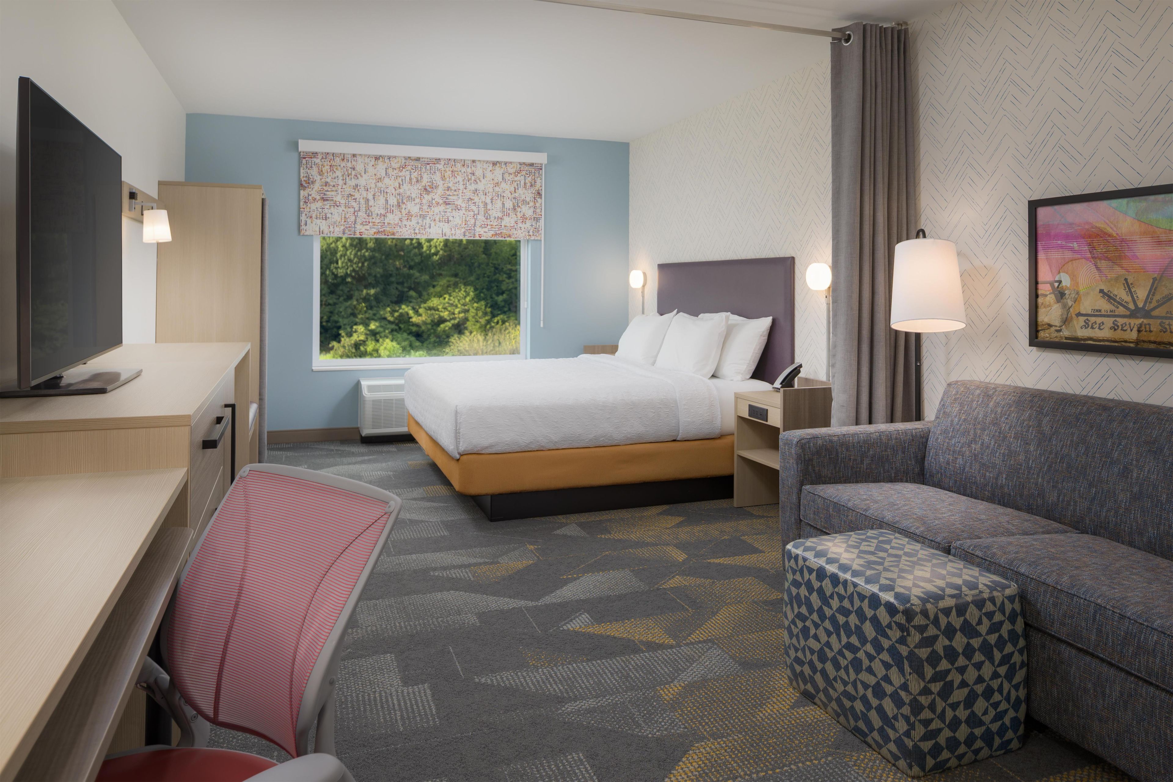 A hotel room with a bed, a desk, a chair, a sofa, and a TV.