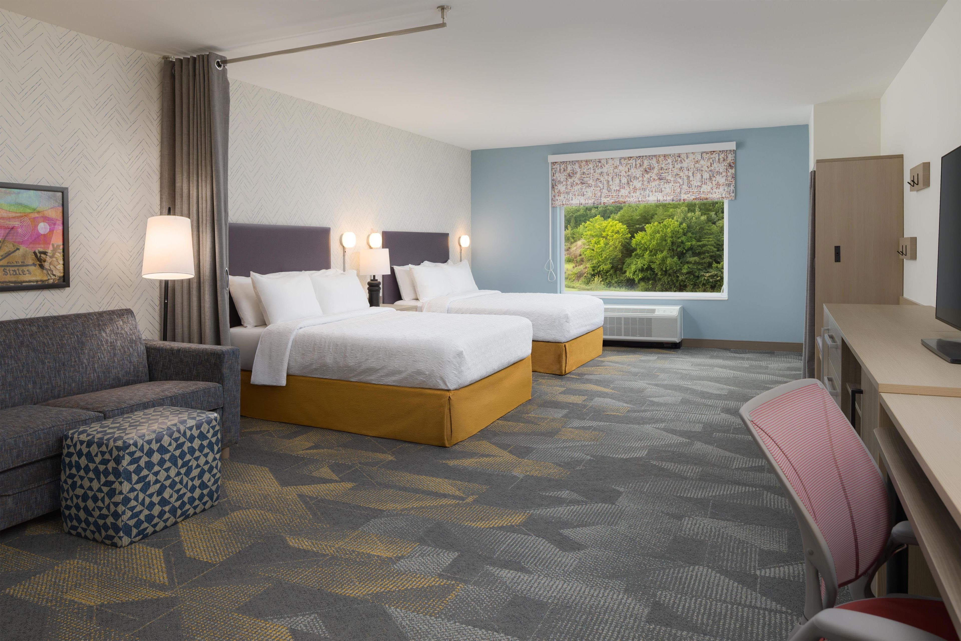 A hotel room with two beds, a sofa, a desk, and a television.