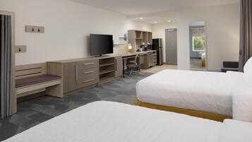 A hotel room with a bed, a desk with a computer, a TV, and a kitchenette.