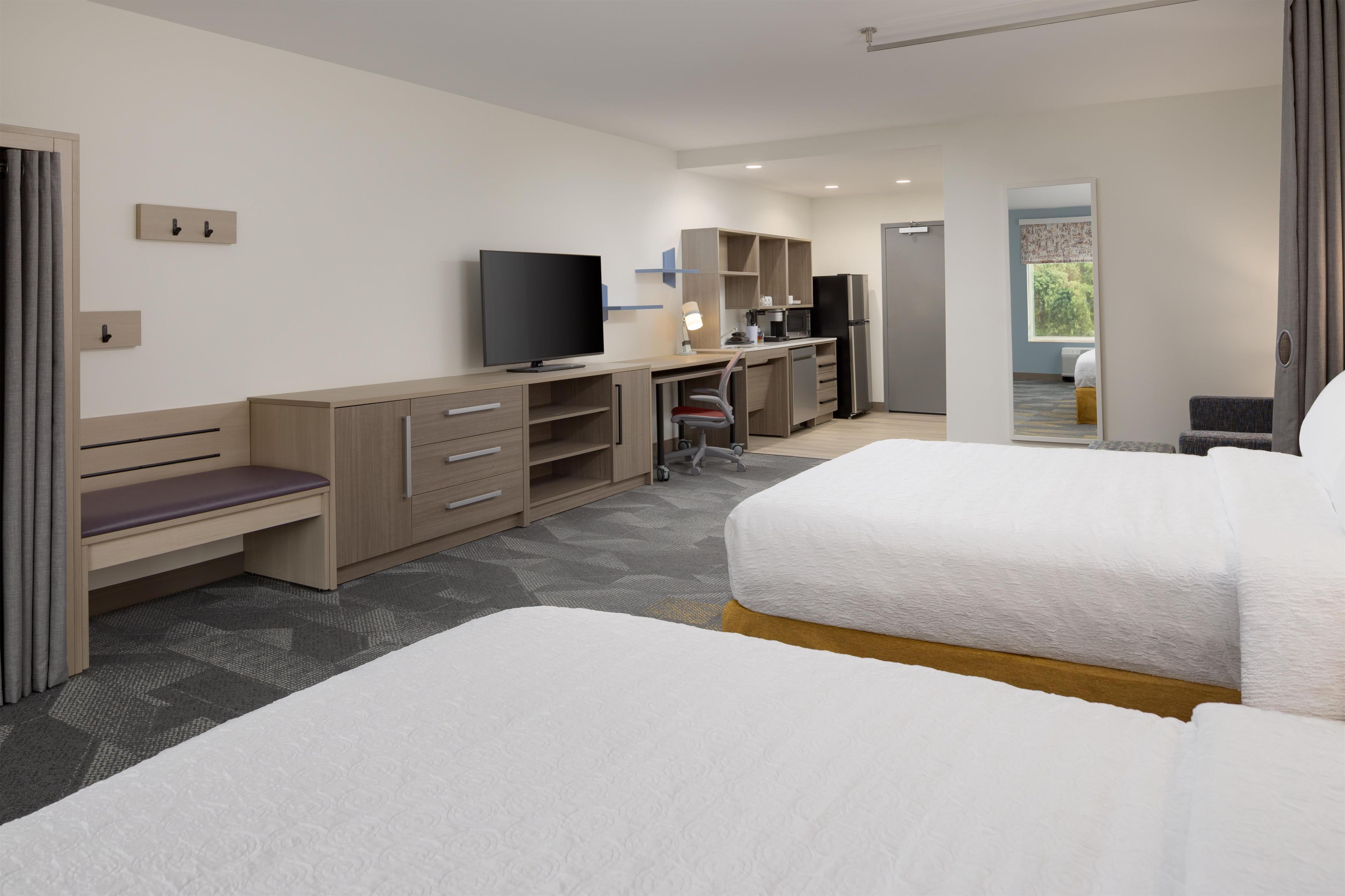A hotel room with a bed, a desk with a computer, a TV, and a kitchenette.