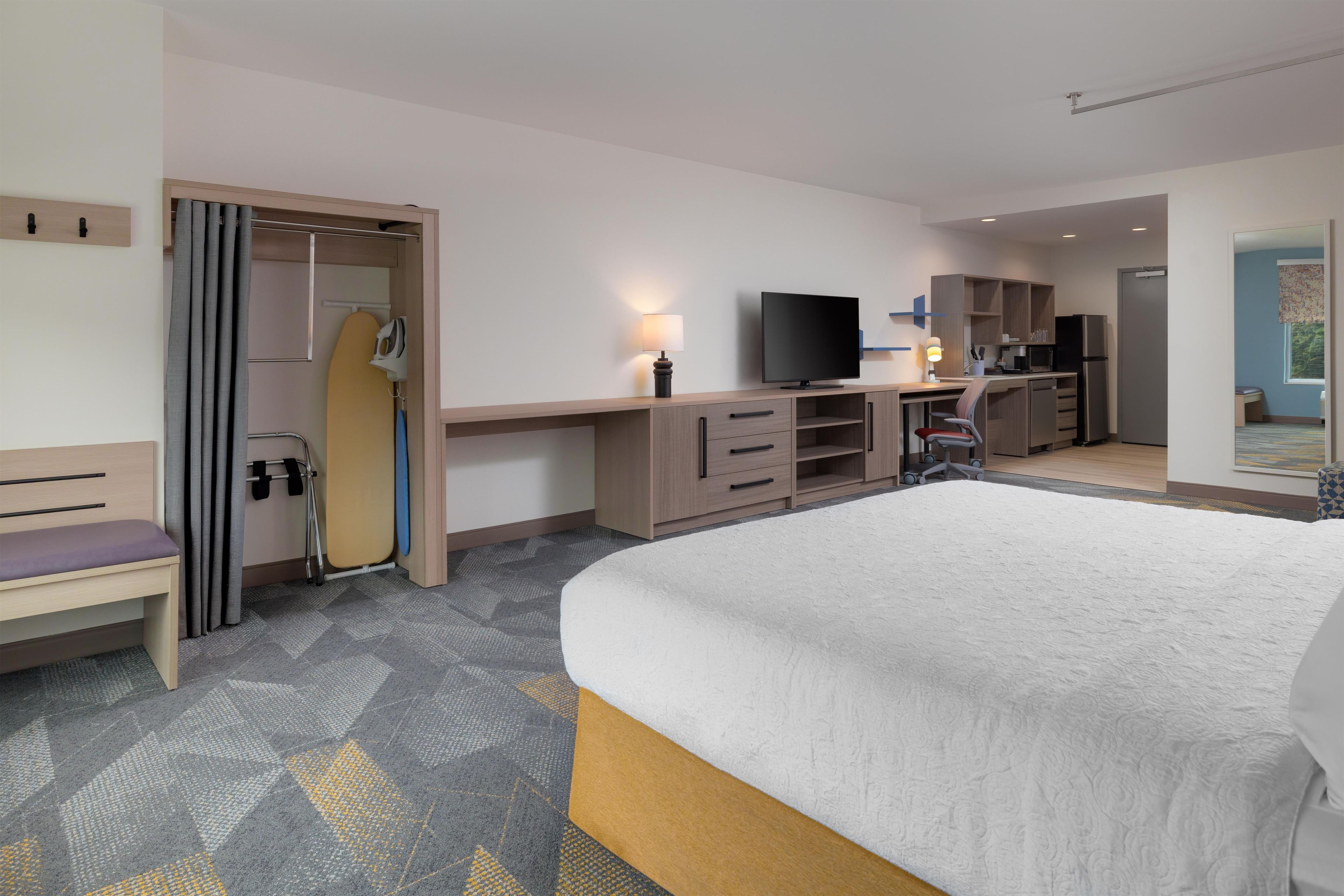 Una habitación de hotel con cama, escritorio, televisor y kitchenette.