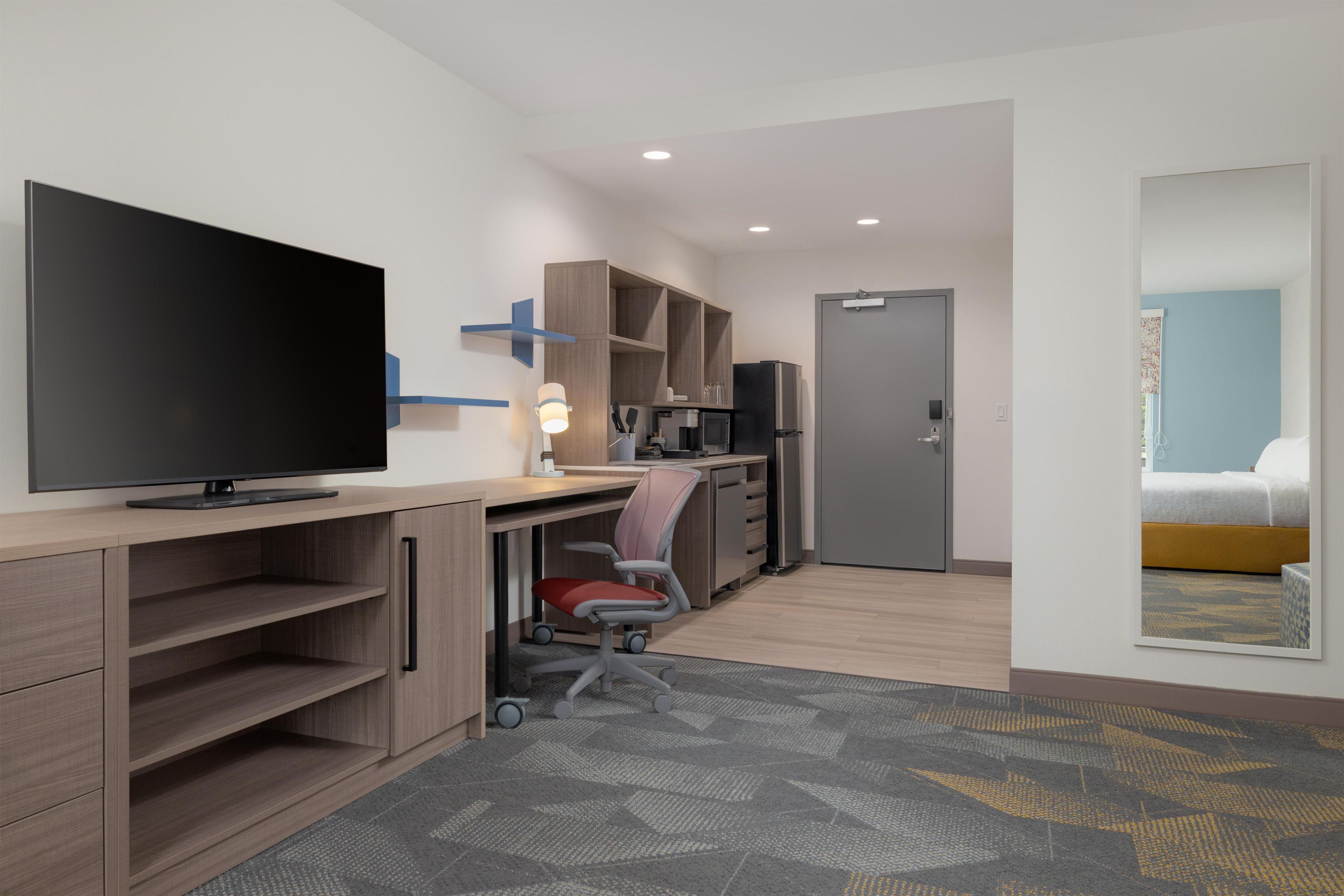 Habitación de hotel moderna con televisión de pantalla plana, escritorio con silla, kitchenette, cama y baño.