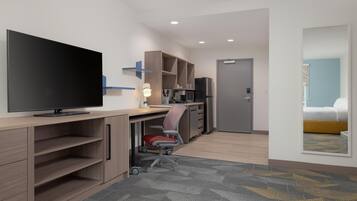 Habitación de hotel moderna con televisión de pantalla plana, escritorio con silla, kitchenette, cama y baño.
