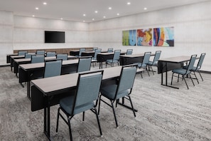 A conference room with multiple tables and chairs, a flat-screen TV mounted on the wall, and abstract art on the back wall.
