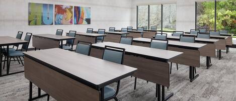 Une salle de conférence dotée de plusieurs tables et chaises, de grandes fenêtres et d’œuvres d’art abstrait accrochées au mur.