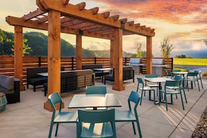 An outdoor patio with wooden pergola, seating, tables, and barbecue grills.