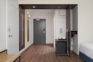 Une chambre d’hôtel avec un lit, un bureau, une bouilloire, un miroir et une porte.