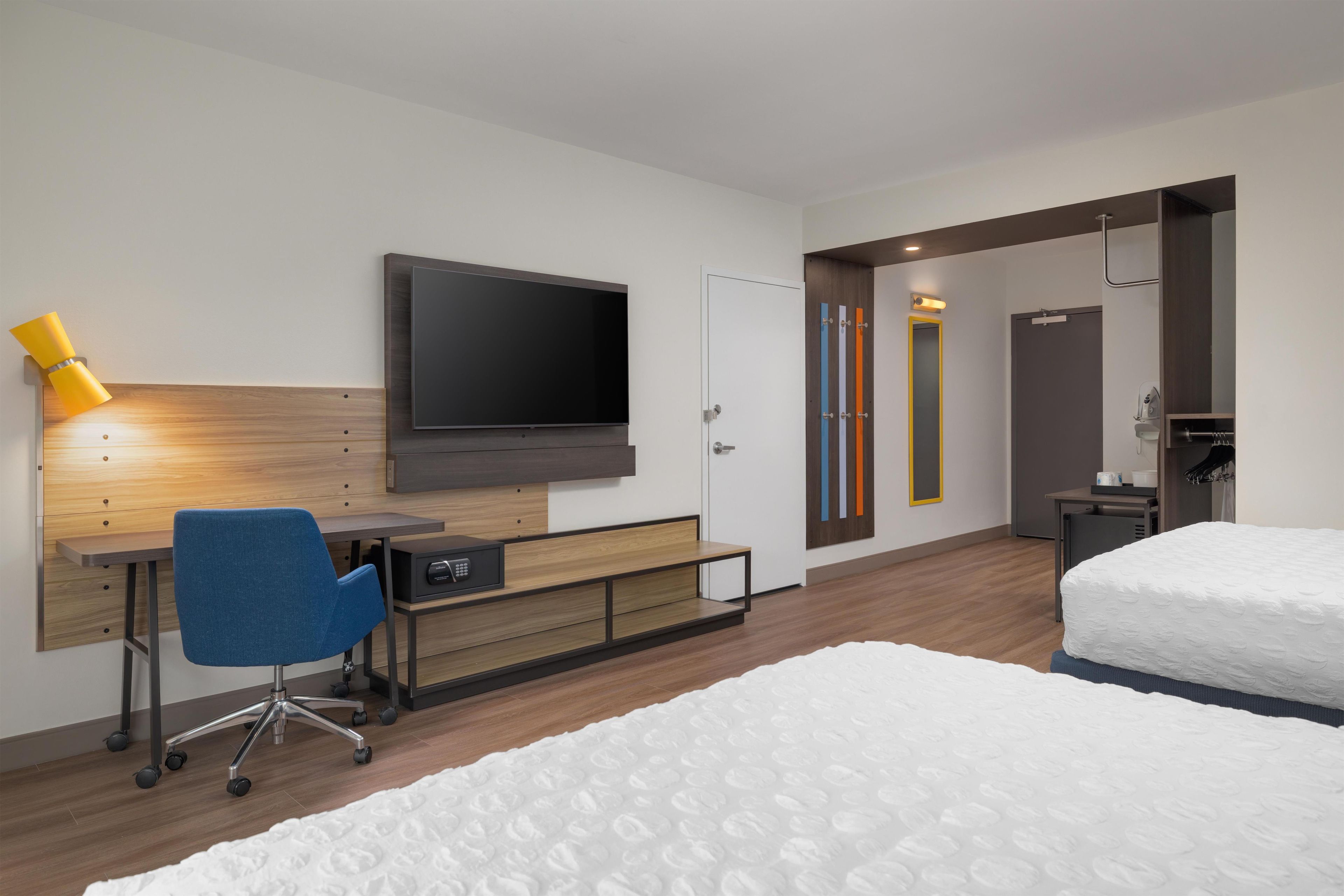 Et moderne hotelværelse med et fladskærms-tv, et skrivebord med stol, en seng og et klædeskab.
