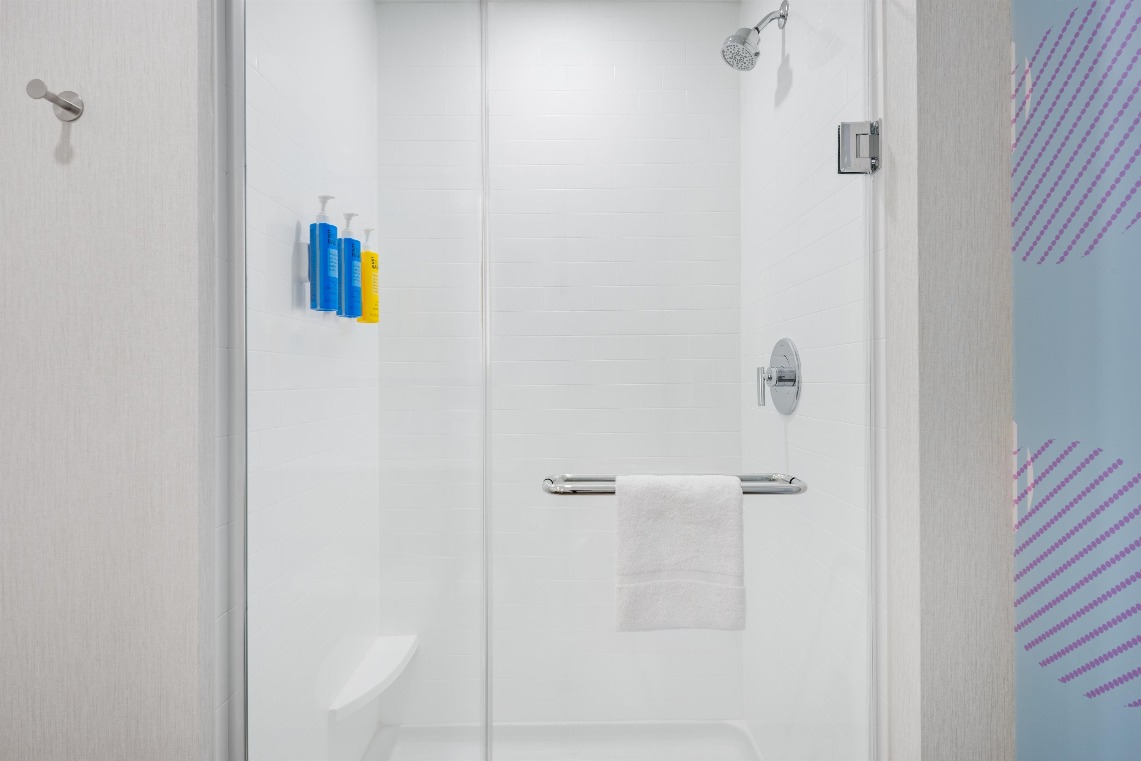Une salle de bain moderne avec une douche à parois de verre, une serviette blanche suspendue à un porte-serviettes et des articles de toilette fixés au mur.