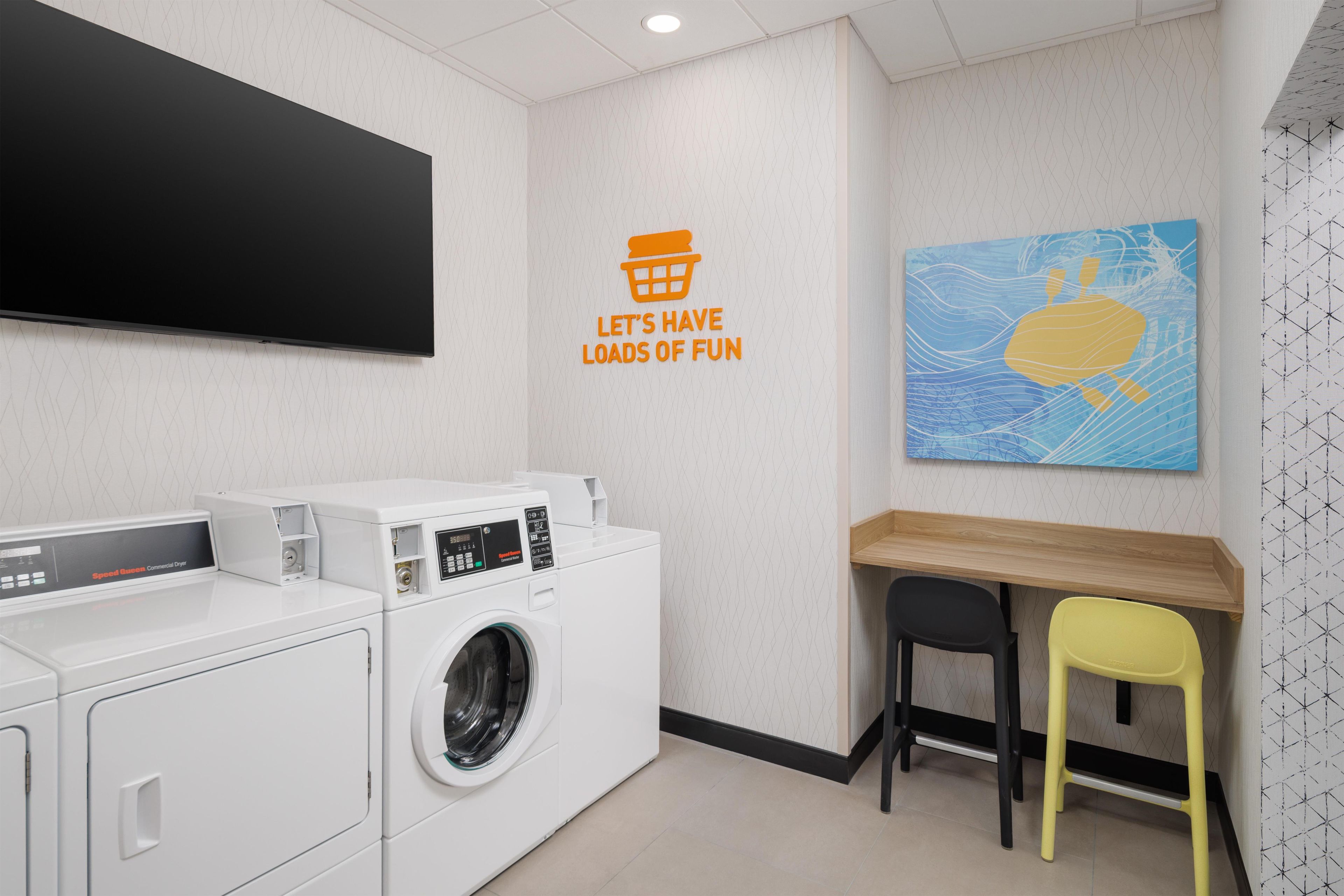 A laundry room with a washing machine, dryer, and a flat-screen TV mounted on the wall.