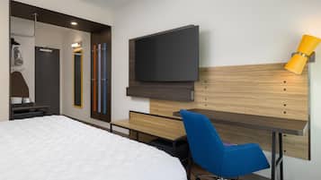Quarto de hotel moderno com cama, escrivaninha, cadeira, televisão e espelho.