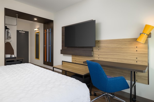 A modern hotel room with a bed, a desk, a chair, a television, and a mirror.