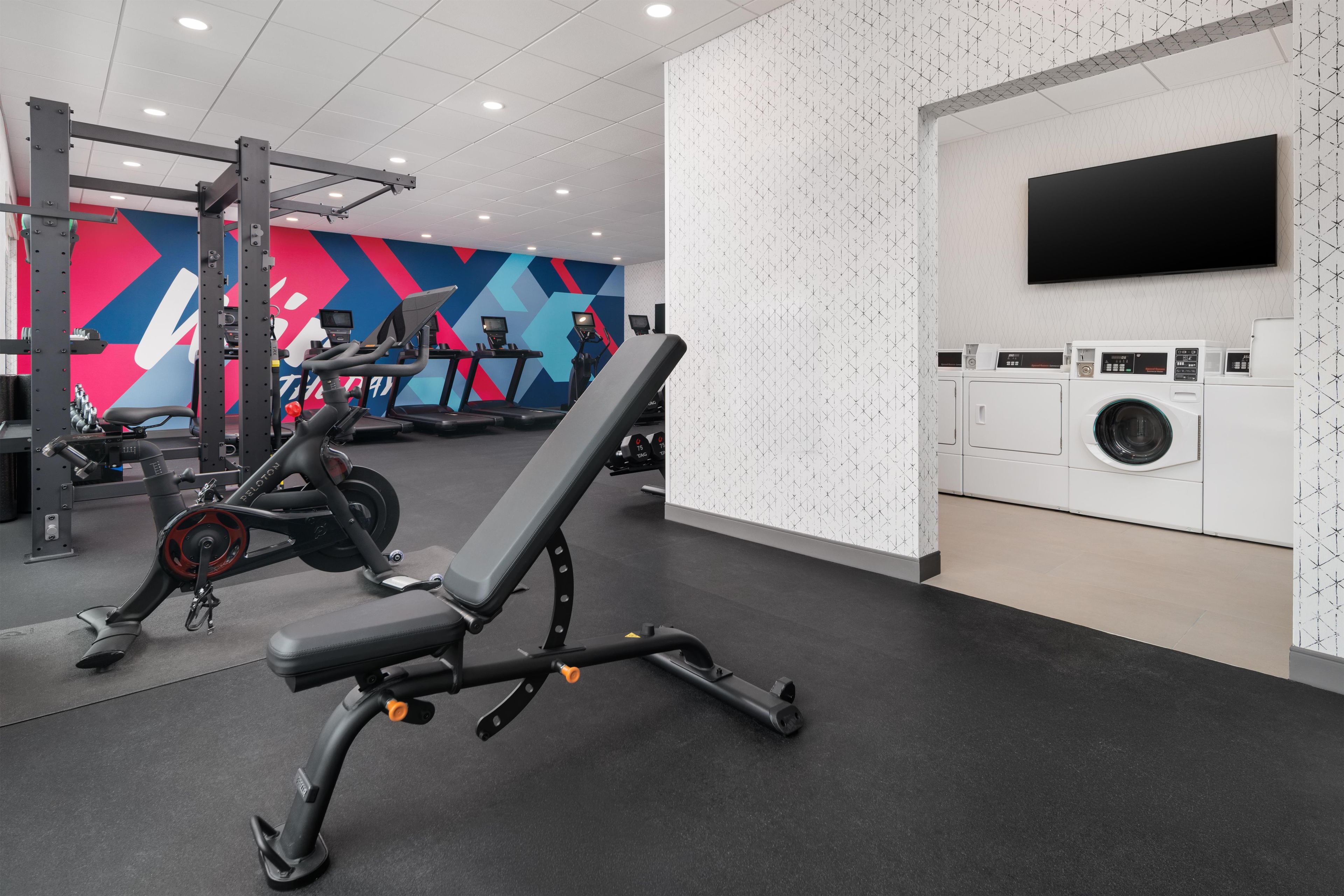A gym with exercise equipment, a wall-mounted TV, and a washing machine.