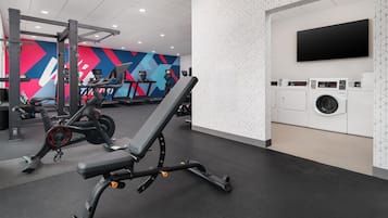 A gym with exercise equipment, a wall-mounted TV, and a washing machine.