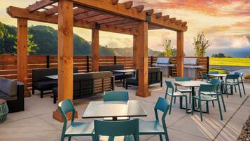 An outdoor patio with wooden pergola, seating, tables, and barbecue grills.