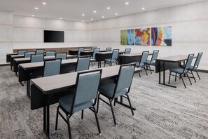 Une salle de conférence dotée de plusieurs tables et chaises, d’un téléviseur à écran plat fixé au mur et d’œuvres d’art abstrait sur le mur du fond.