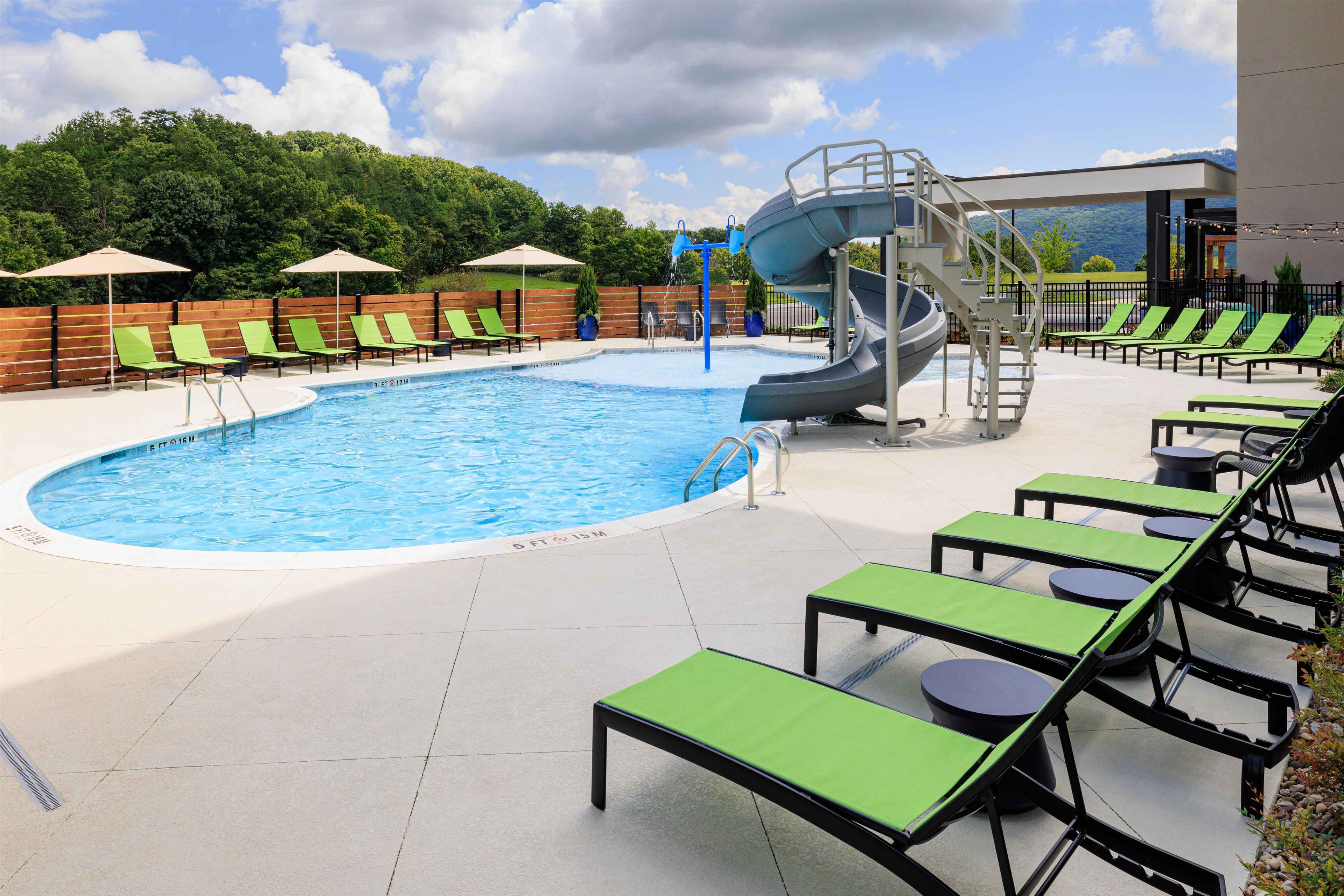 A swimming pool with a water slide, lounge chairs, and a view of the mountains.