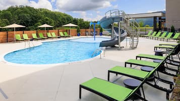 A swimming pool with a water slide, lounge chairs, and a view of the mountains.