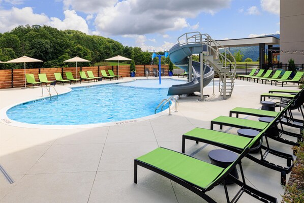 A swimming pool with a water slide, lounge chairs, and a view of the mountains.