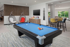 A pool table with balls, two hanging chairs, a television, and a bar area with chairs.