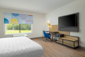 Habitación de hotel con cama, escritorio, silla, televisor y ventana con vista a áreas verdes.