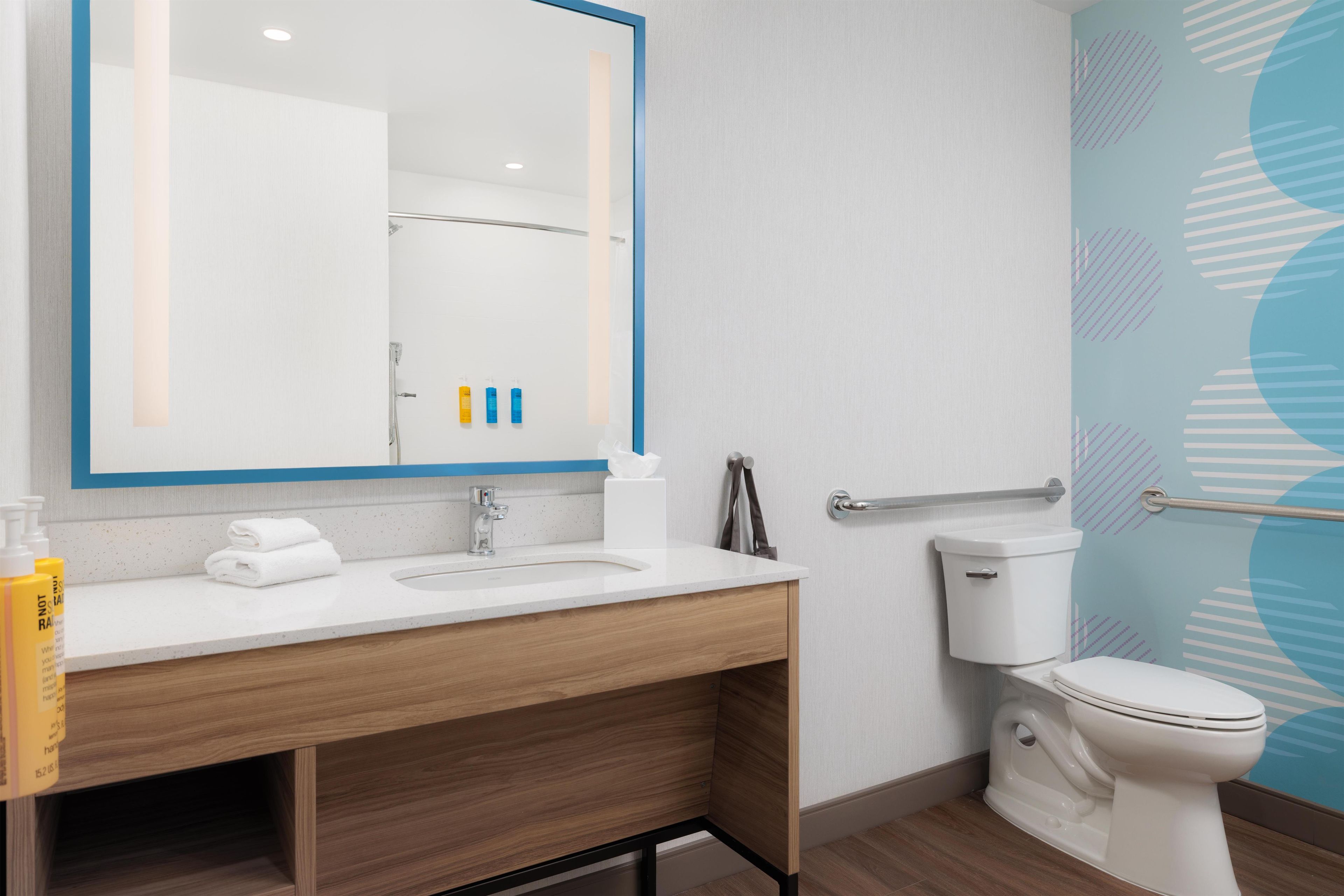 A modern bathroom with a white sink, mirror, and toilet. There are toiletries on the counter and a towel rack.