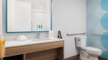 A modern bathroom with a white sink, mirror, and toilet. There are toiletries on the counter and a towel rack.
