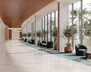 Un vestíbul d'hotel modern amb un llarg passadís, columnes de marbre i cadires tapissades de verd.