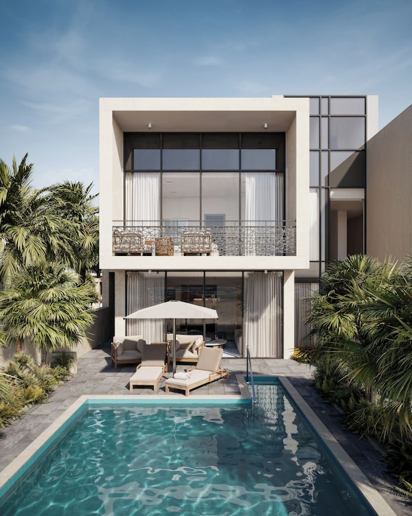 Un edifici modern de dos pisos amb piscina, mobiliari exterior i plantes tropicals.