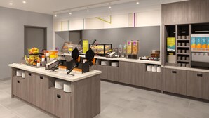 Um balcão de café da manhã moderno com máquinas de waffle, um painel digital de cardápio e diversos dispensadores de alimentos e bebidas.