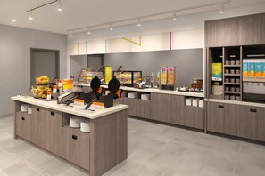 Una barra de desayuno moderna con máquinas para gofres, una pantalla digital con el menú y diversas opciones de dispensadores de comida y bebidas.