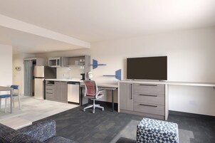 Un espacio habitable compacto con kitchenette, comedor, sofá y televisor.