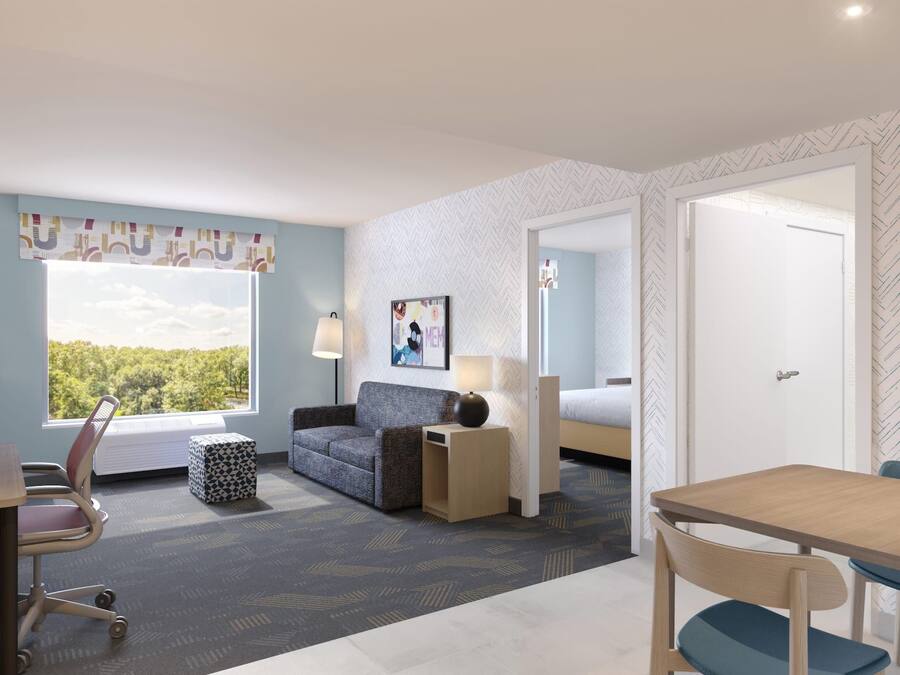 Ein Hotelzimmer mit Bett, Schreibtisch, Stuhl, Sofa, Lampe und einem Fenster mit Blick auf Bäume.