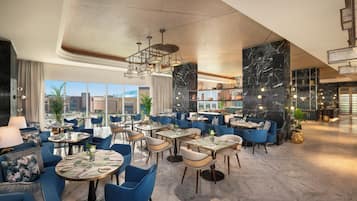 A modern restaurant interior with round tables, blue chairs, and a view of the cityscape through large windows.