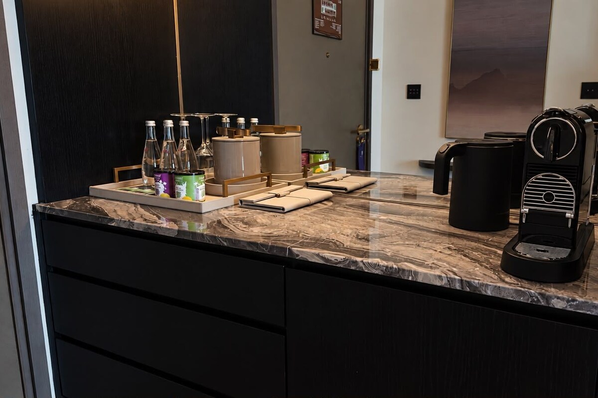 Zona de recepció d'hotel amb un mostrador de marbre, una màquina de cafè i diverses comoditats, com ara ampolles i envasos.