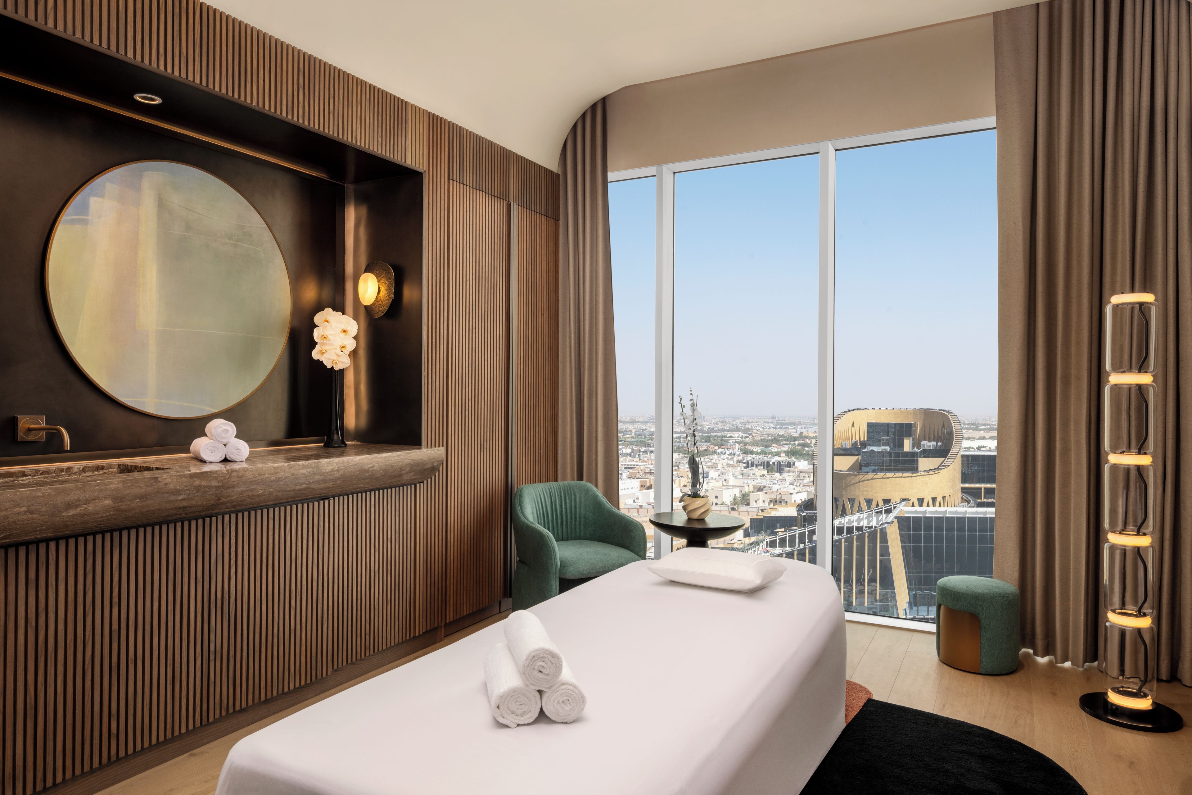 A hotel room with a large bed, a sitting area, a view of the city, and a large mirror.