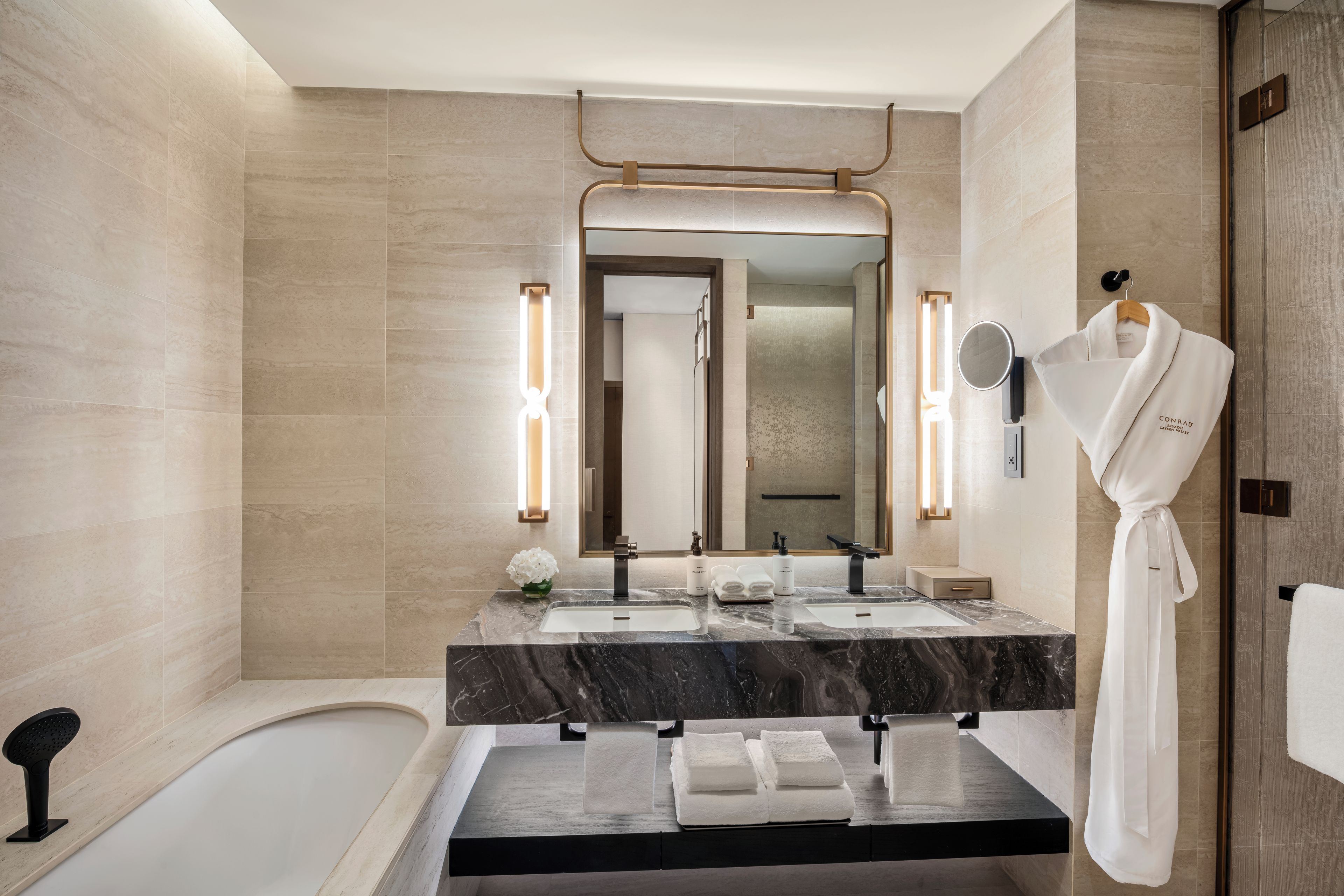 A modern bathroom with a bathtub, a vanity with a mirror, and a robe hanging on a hook.