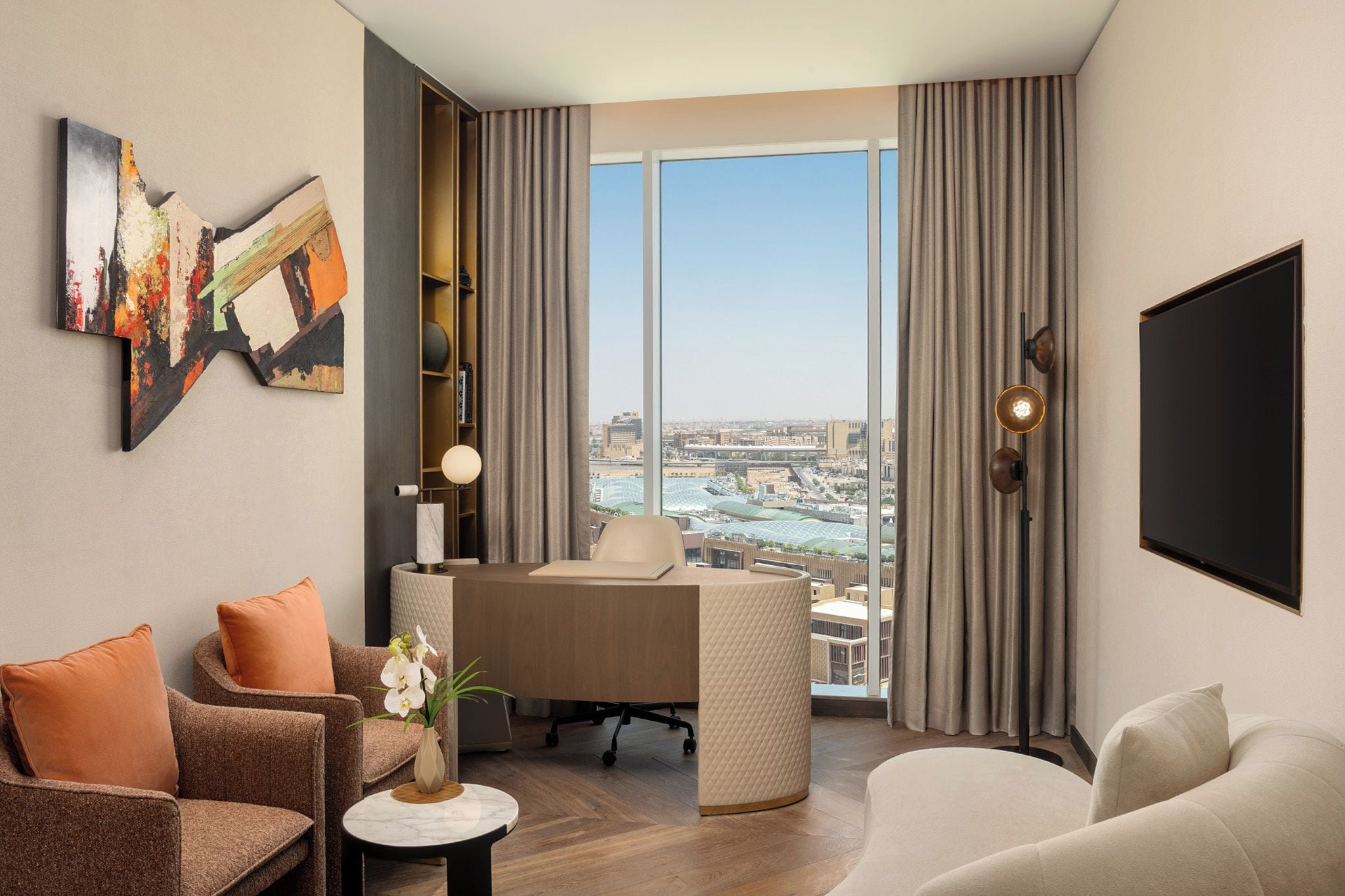 A modern hotel room with a large window, a desk, a sofa, and a TV.