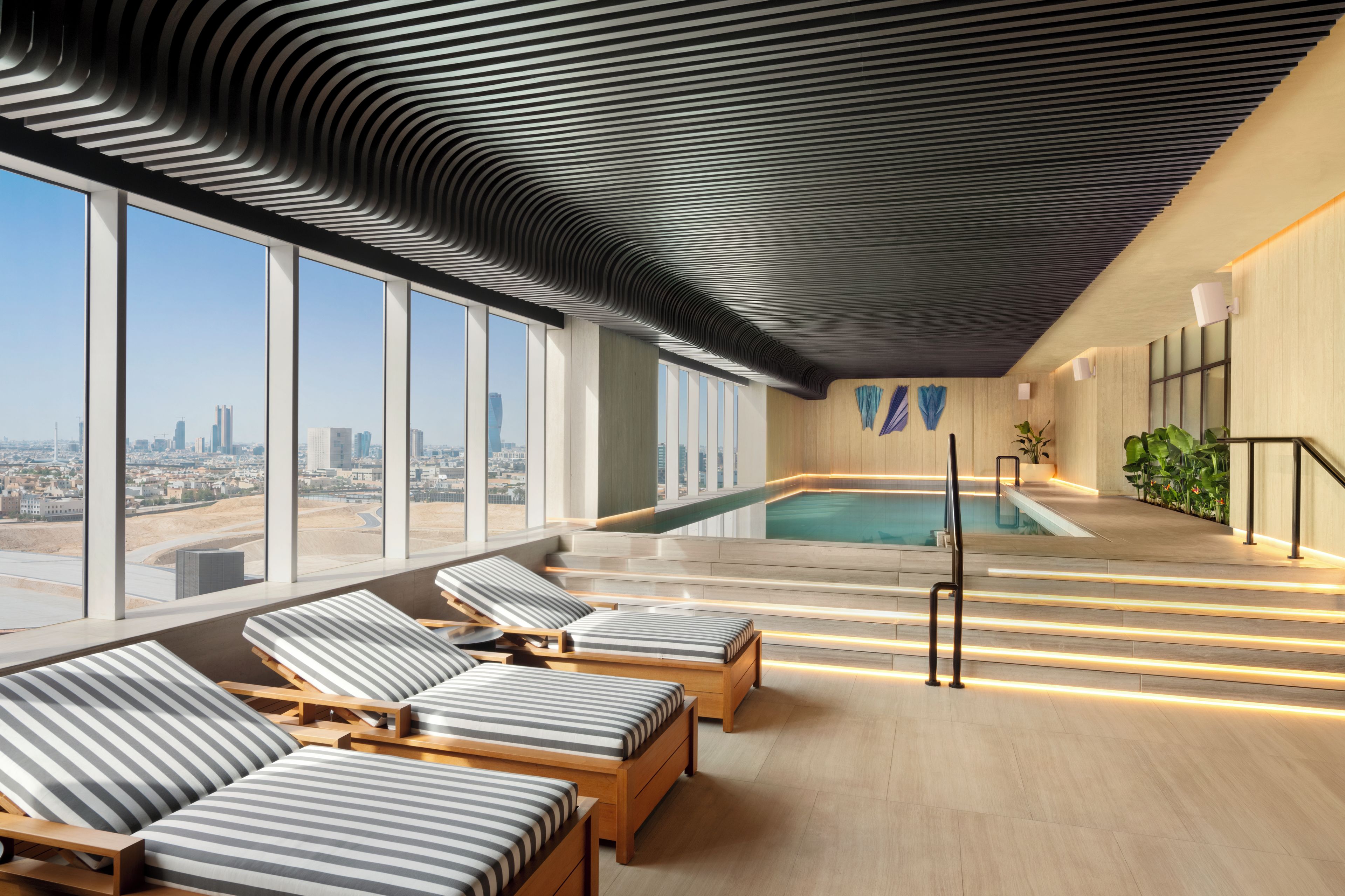 A modern indoor pool area with lounge chairs and a view of the cityscape.