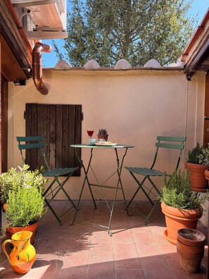 Un patio con tavolo e due sedie, circondato da piante in vaso e una rustica porta in legno.