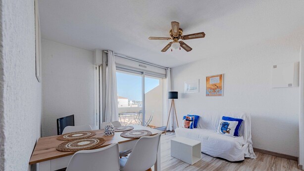 A room with a dining table, chairs, a bed, a ceiling fan, and a window with a view. - Marine de port, boats and relaxation (Canet-en-Roussillon)