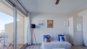 A room with a bed, a standing lamp, a small table, and a window with a view of the outside. - Marine de port, boats and relaxation (Canet-en-Roussillon)